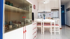 A modern kitchen with white cabinets, a dining table with chairs, and a glass-fronted cupboard with dishes. - Nice Apartment With Sunny Terrace in Bibione (San Michele al Tagliamento)