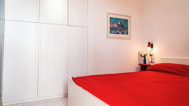 A bedroom with a bed, a nightstand, a framed picture on the wall, and a wardrobe. - Nice Apartment With Sunny Terrace in Bibione (San Michele al Tagliamento)