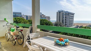 A balcony with a white table and chairs, a bicycle, and a view of the sea and hotel buildings. - Nice Apartment With Sunny Terrace in Bibione (San Michele al Tagliamento)