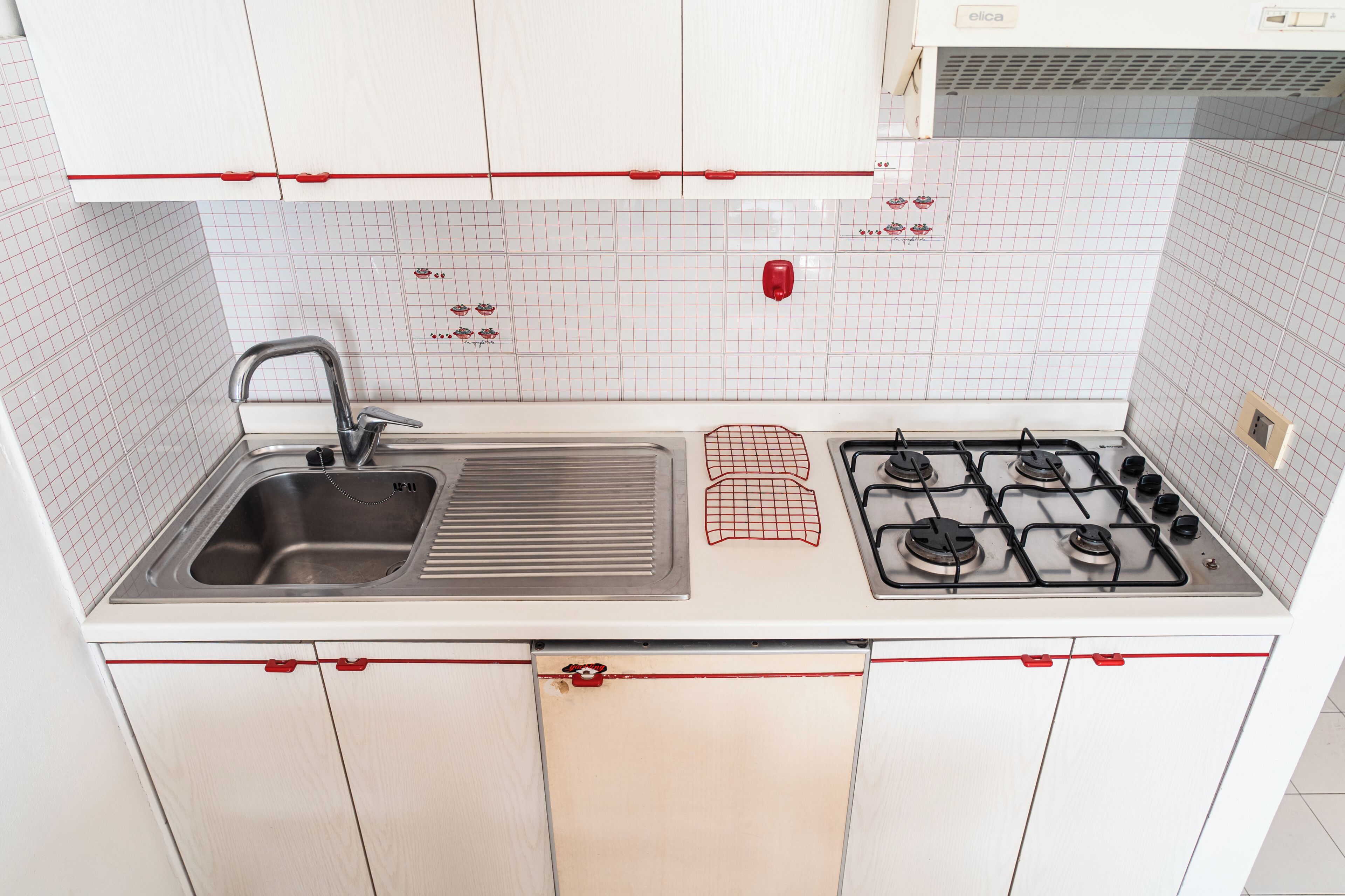 A kitchen with a sink, stove, and white cabinets with red handles.