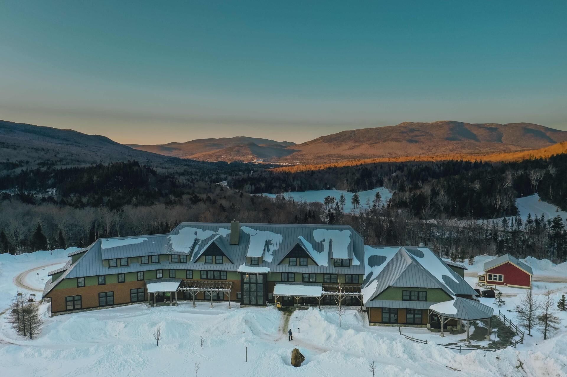 Un gran lodge con varias construcciones, un paseo techado y vistas a montañas nevadas.