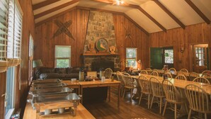 A rustic dining area with wooden tables and chairs, a stone fireplace, and a lofted ceiling with exposed beams. - Cabin, Double Bed, 2 Bunks, Shared Bathroom (Blairstown)