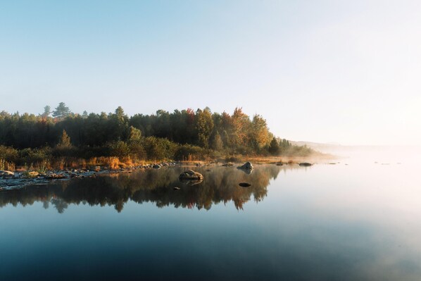 Un lac paisible, bordé d’une forêt, dont les eaux reflètent clairement le paysage.