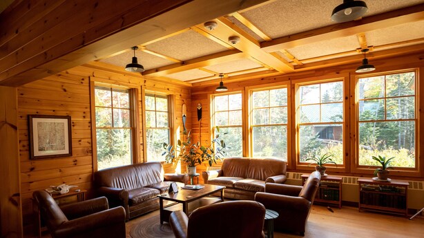 L’intérieur chaleureux d’un chalet avec des murs en bois, de grandes fenêtres, des meubles en cuir et une cheminée.