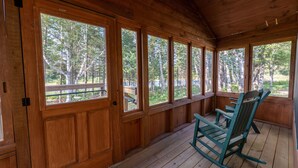 Une cabane en bois dotée de grandes fenêtres et d’un fauteuil à bascule.