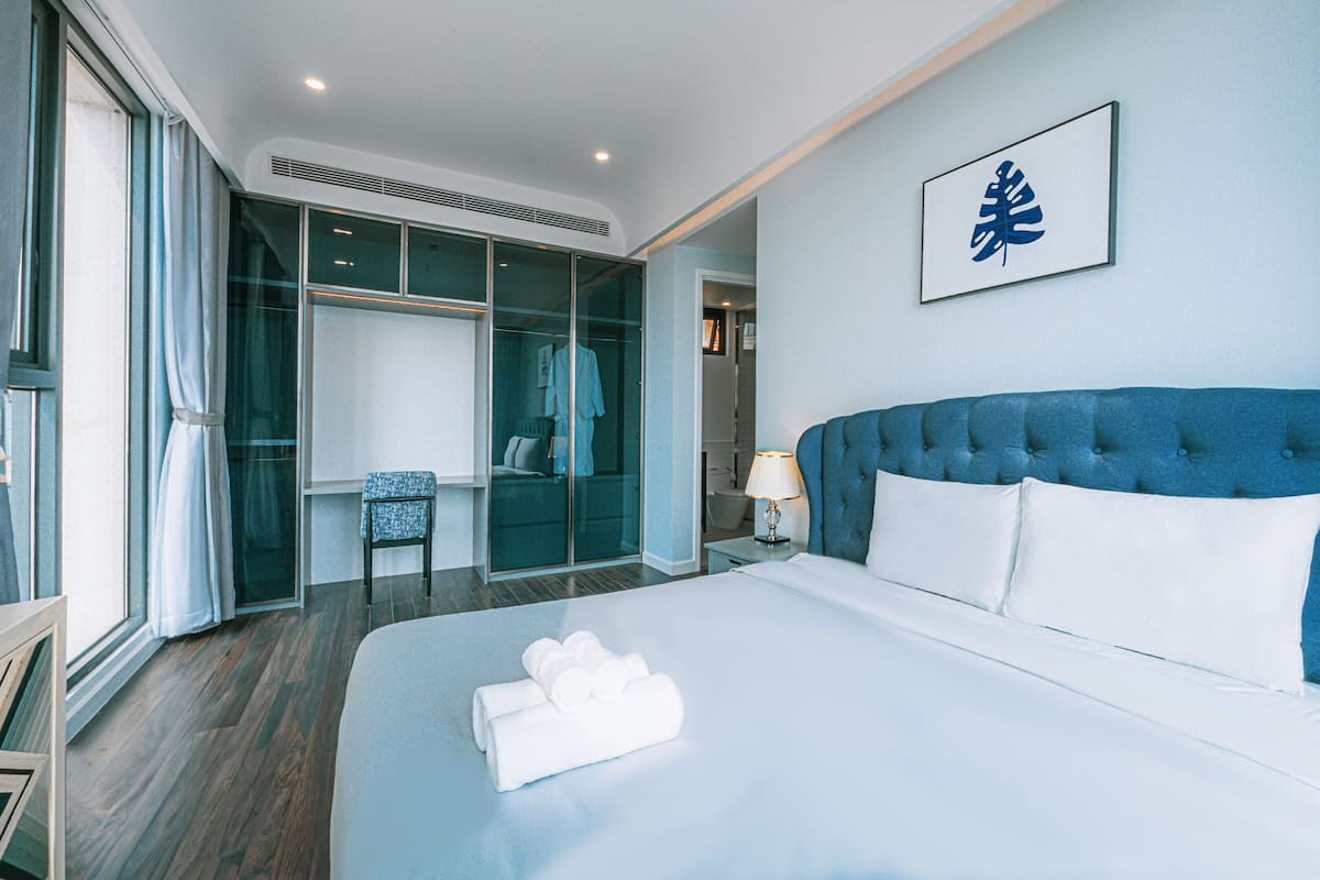 A hotel room with a large bed, a wardrobe, a seating area, and a bathroom visible through a glass door.