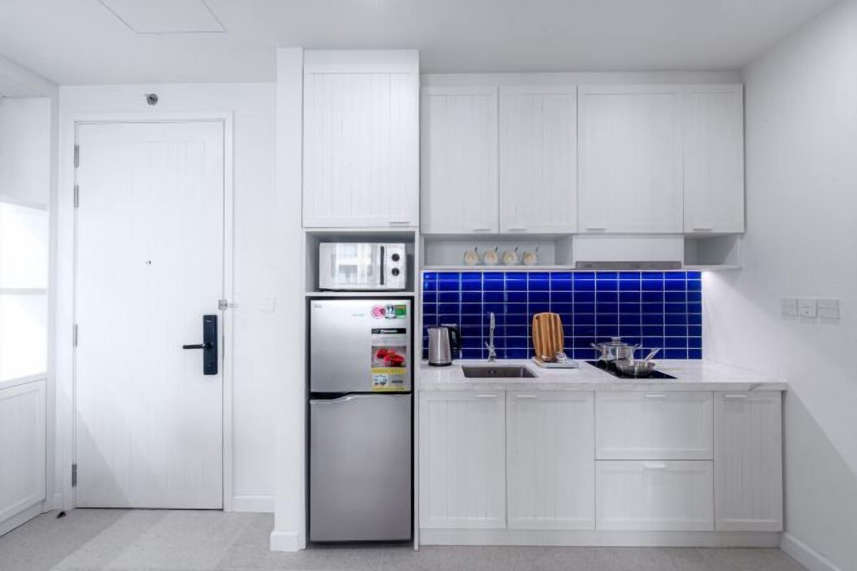A modern kitchen with white cabinets, a stainless steel refrigerator, and a blue-tiled backsplash.