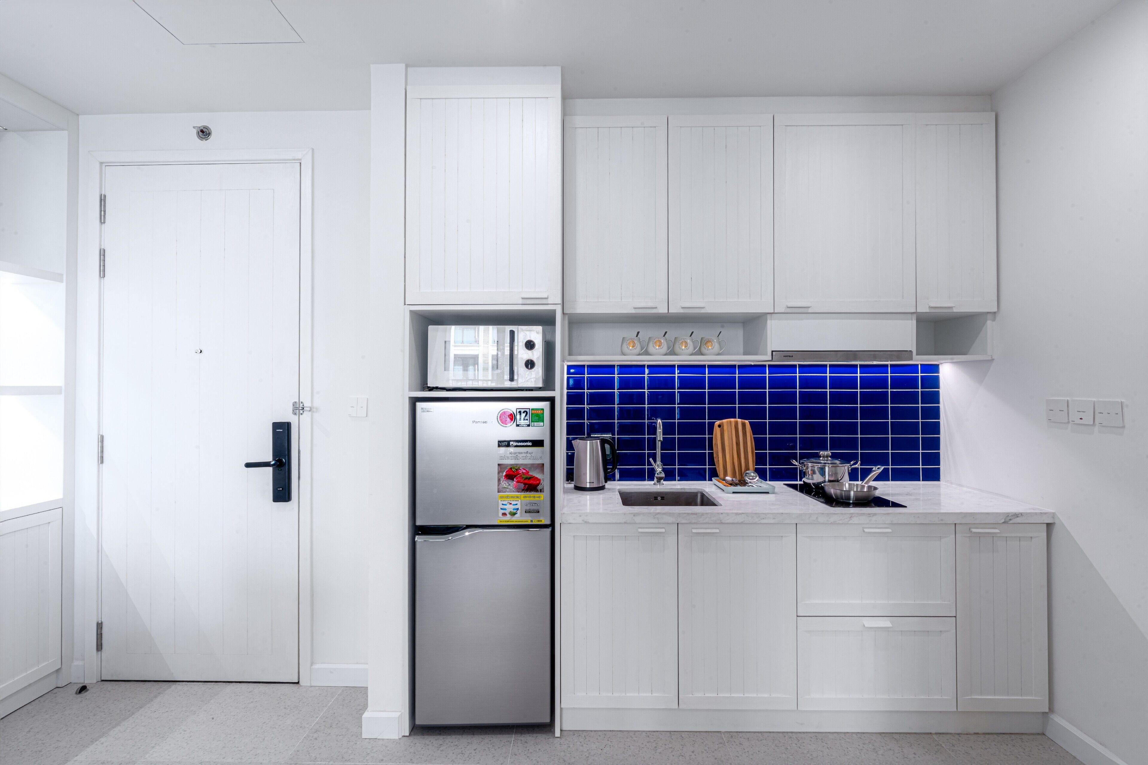 A modern kitchen with white cabinetry, a stainless steel refrigerator, a blue tiled backsplash, and a sink.