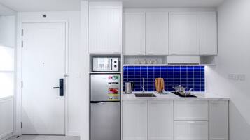 A modern kitchen with white cabinetry, a stainless steel refrigerator, a blue tiled backsplash, and a sink.