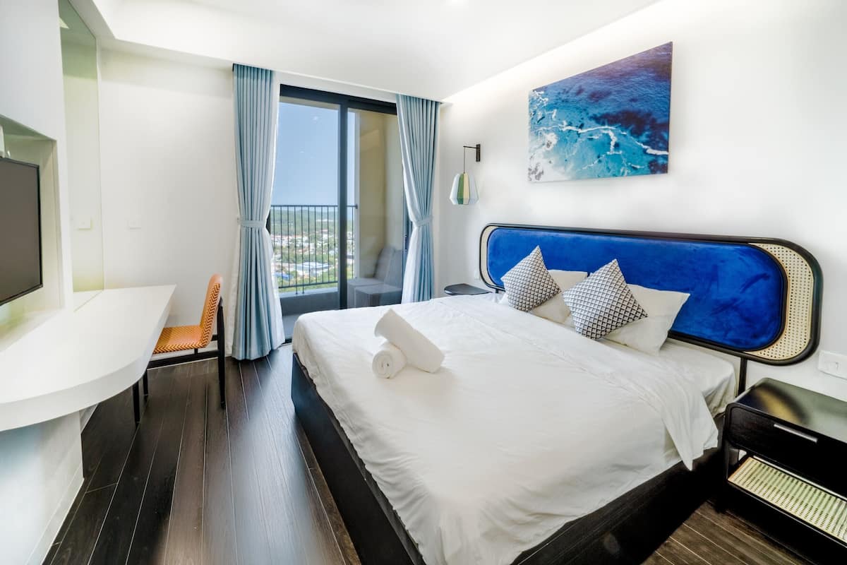 A hotel room with a bed, a desk, a chair, and a large window with a view.
