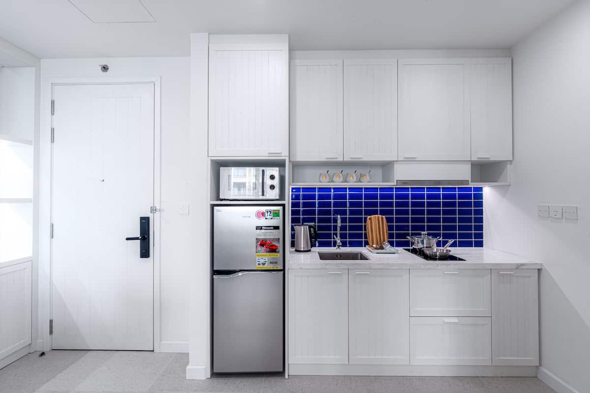 A modern kitchen with white cabinetry, a stainless steel refrigerator, a blue-tiled backsplash, and a sink with a kettle.