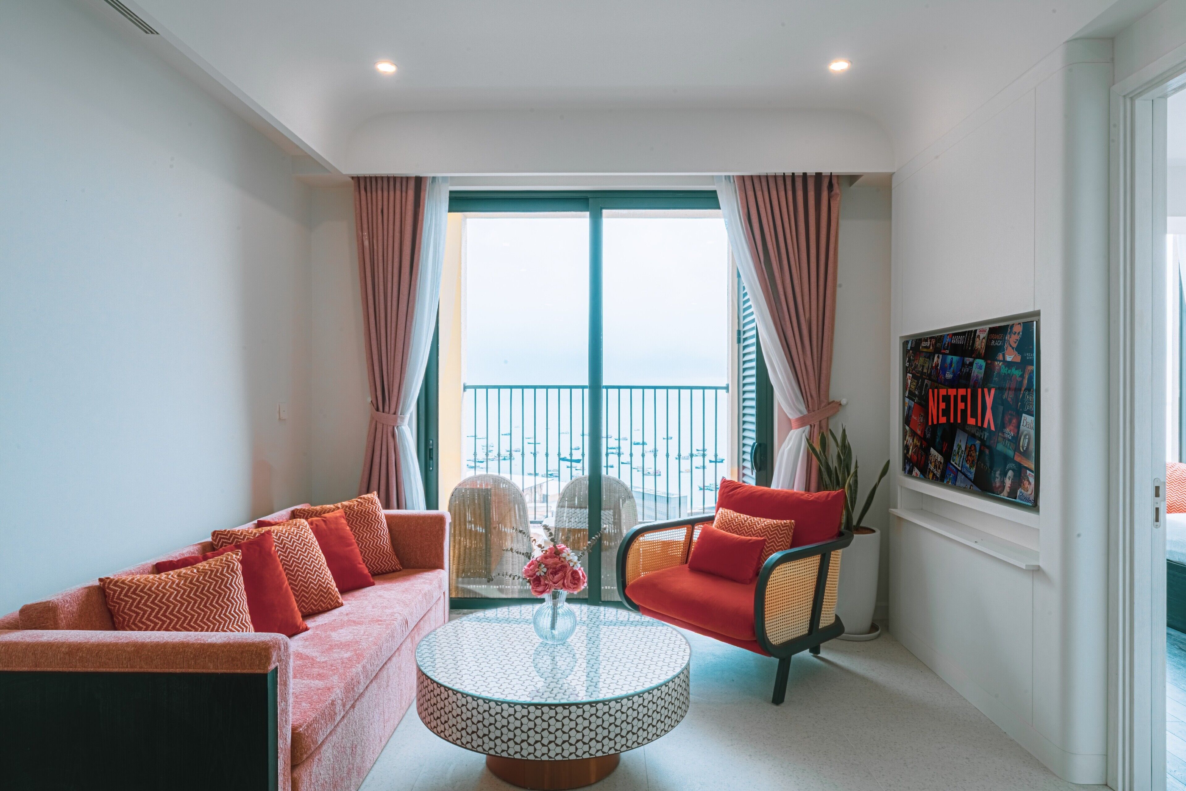A modern living room with a sofa, armchair, and coffee table. A large window with curtains and a view of the city is visible.