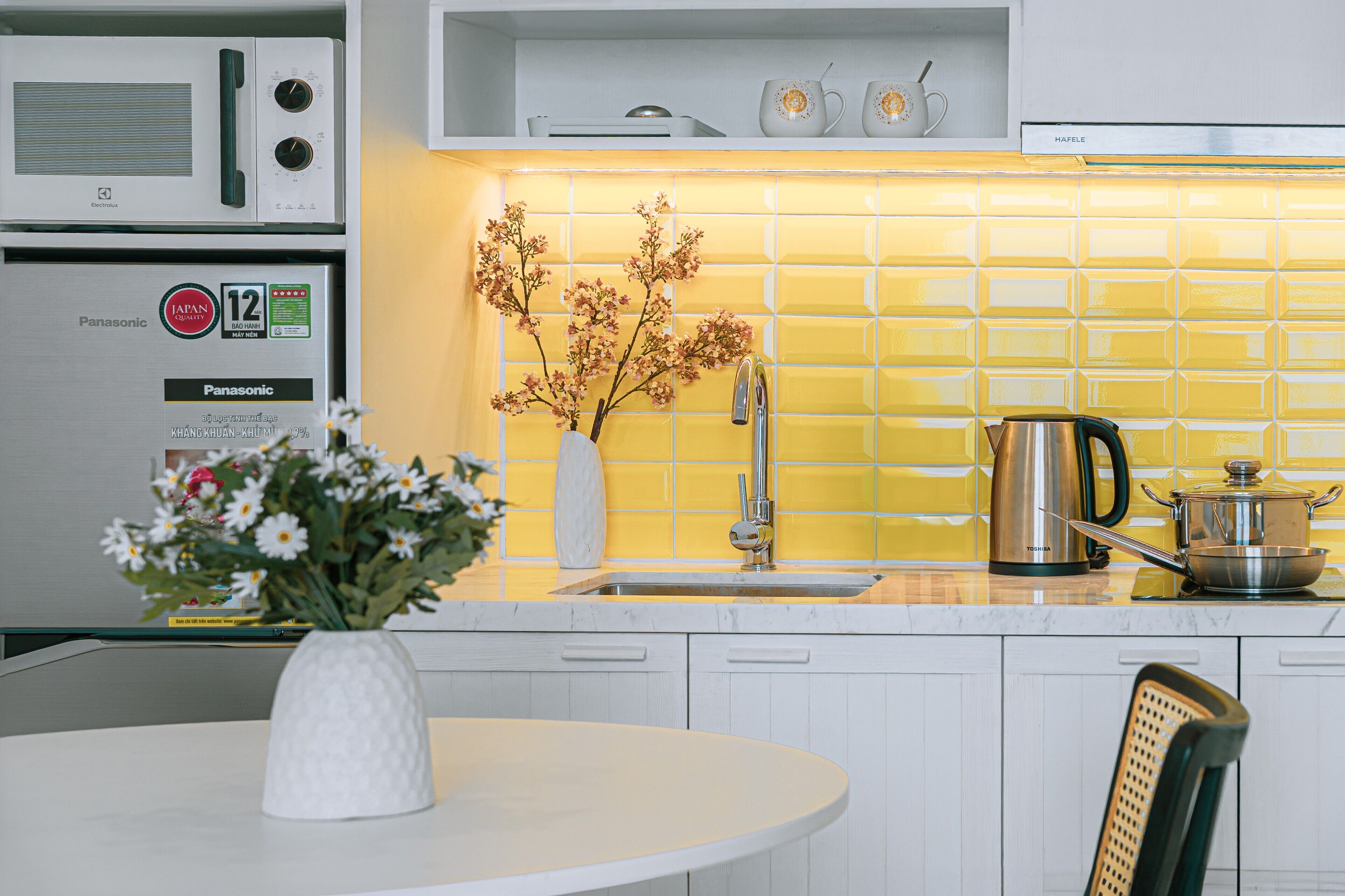 A kitchen with a microwave, refrigerator, sink, and a vase with flowers on the counter.