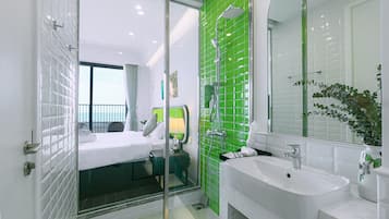 Un baño de hotel moderno con un espejo grande, un lavabo blanco y una zona de ducha.