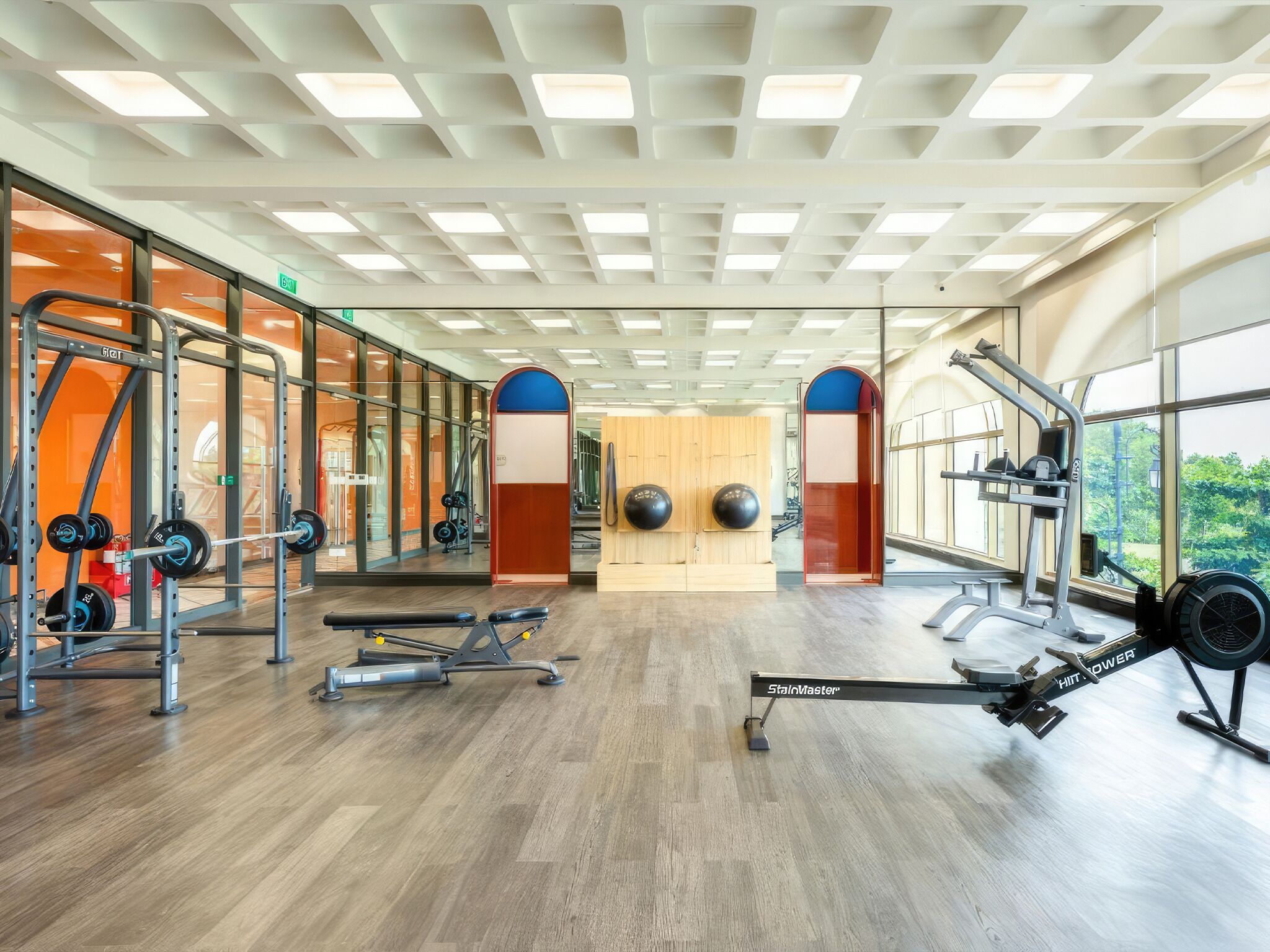 Uma academia com equipamentos de musculação, paredes espelhadas e amplas janelas.