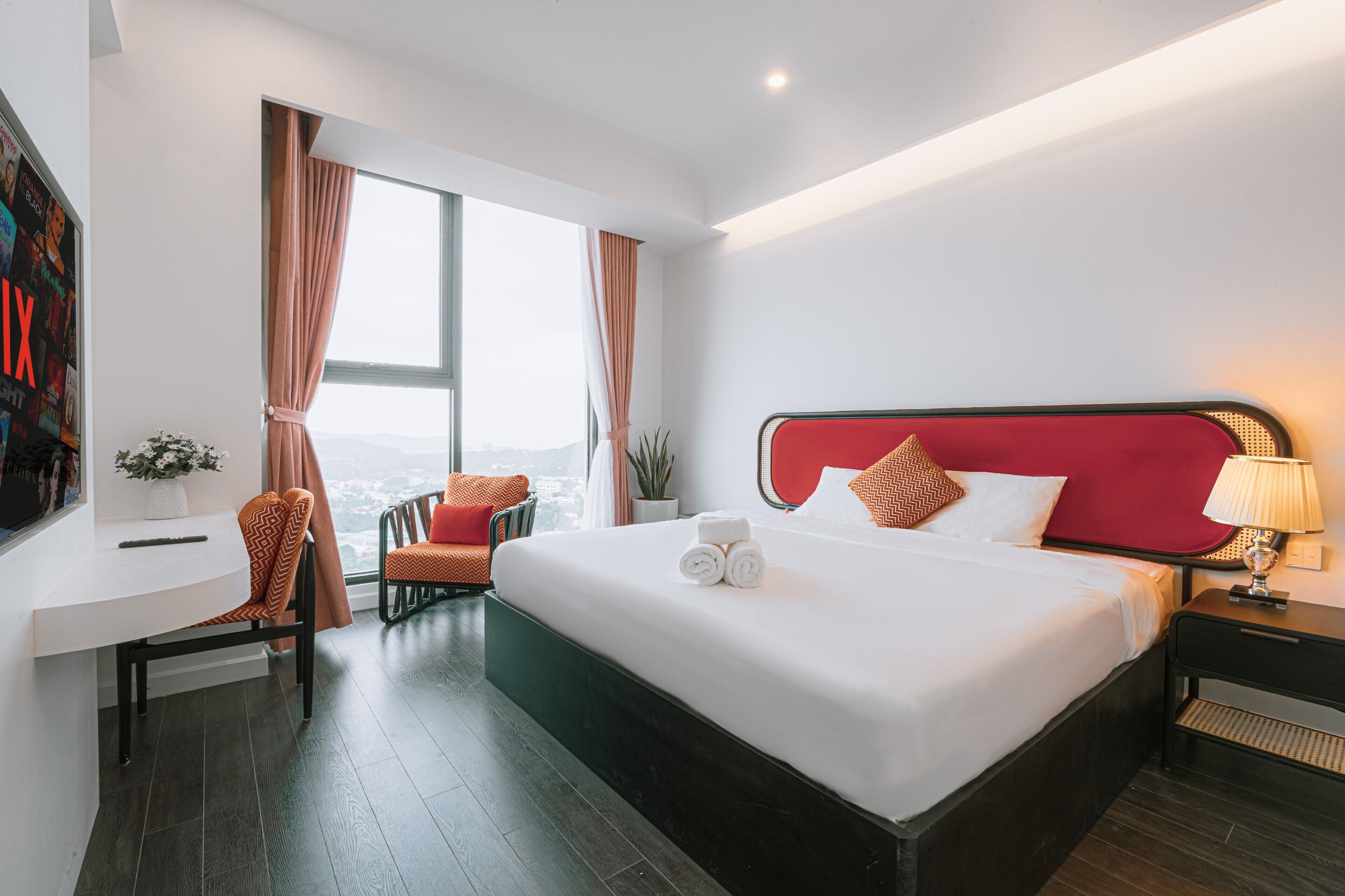 A modern hotel room with a large bed, a desk, and a view of the city.