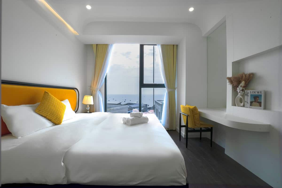 A hotel room with a large bed, a chair, a small table, and a view of the city.