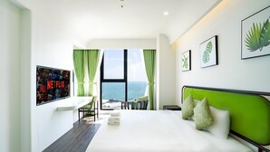 A modern hotel room with a large bed, a desk, and a view of the ocean.