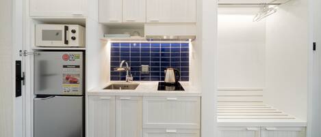 A compact kitchen with white cabinetry, a microwave, a coffee maker, and a blue tiled backsplash.