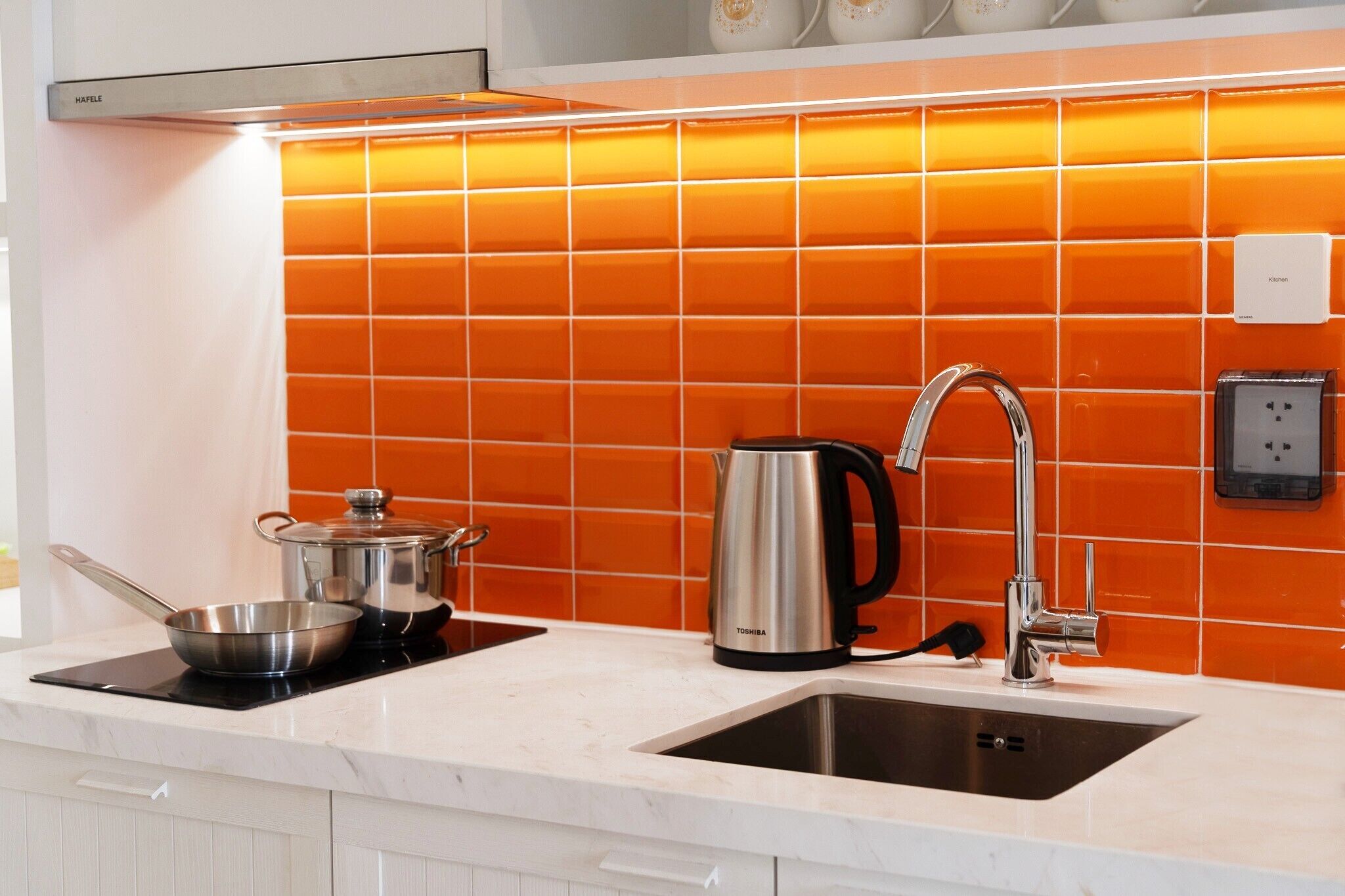A kitchen with a modern design, featuring a stainless steel kettle, a pot, and a kettle on a black induction cooktop.