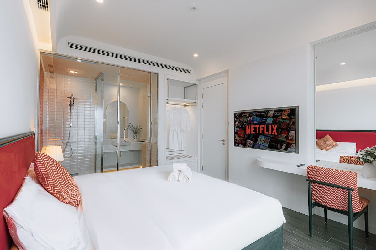 A hotel room with a bed, a desk, a shower, and a wall-mounted TV displaying the Netflix logo.