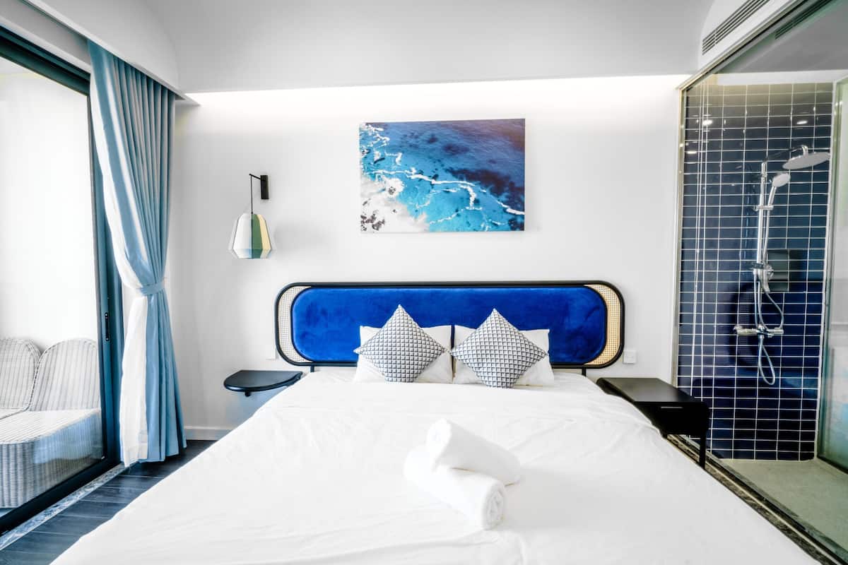 A hotel room with a bed, a painting, a shower, and a view of the sea.