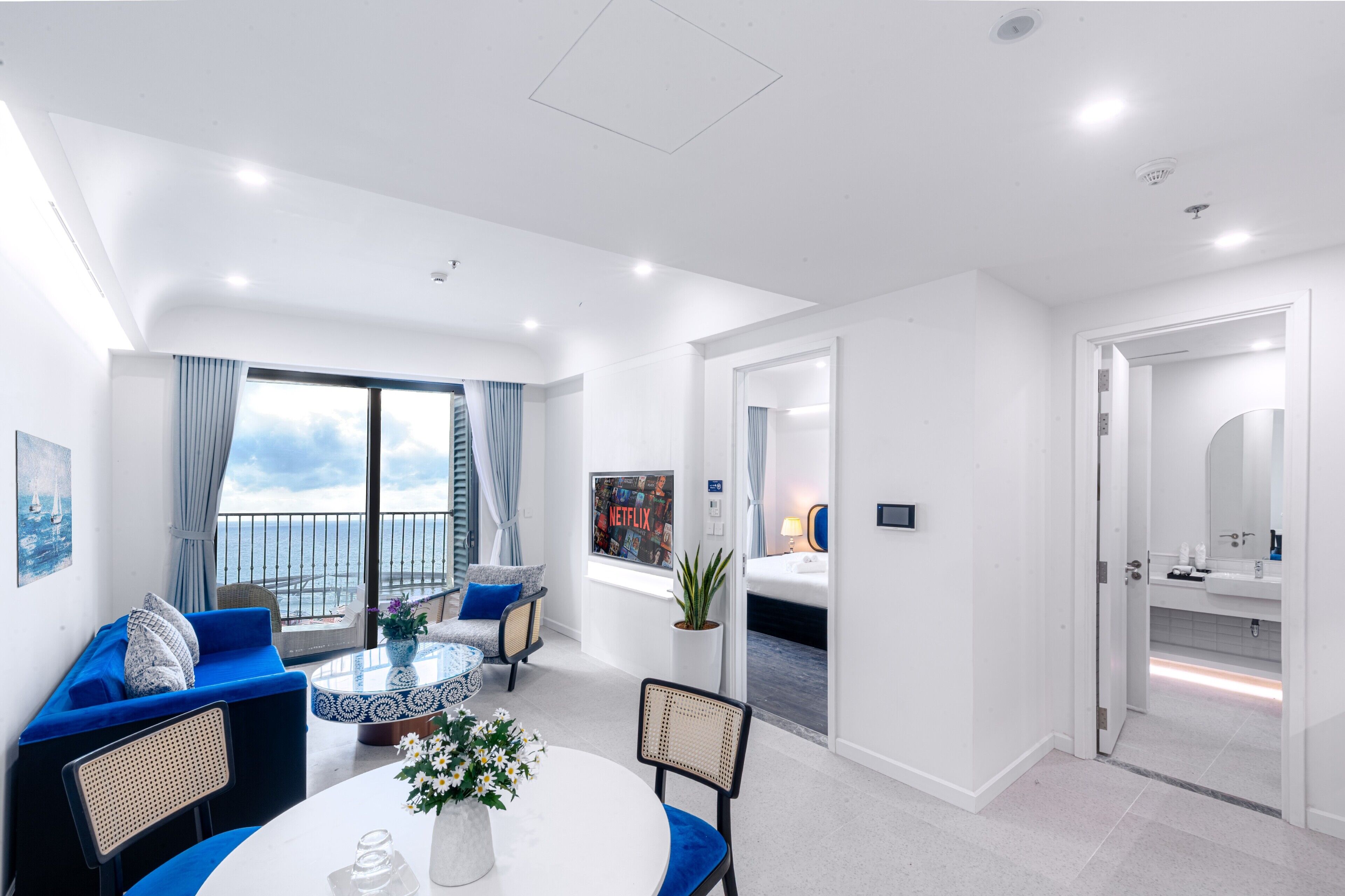 Una habitación de hotel moderna con balcón, una zona de comedor con una mesa redonda y un baño independiente.