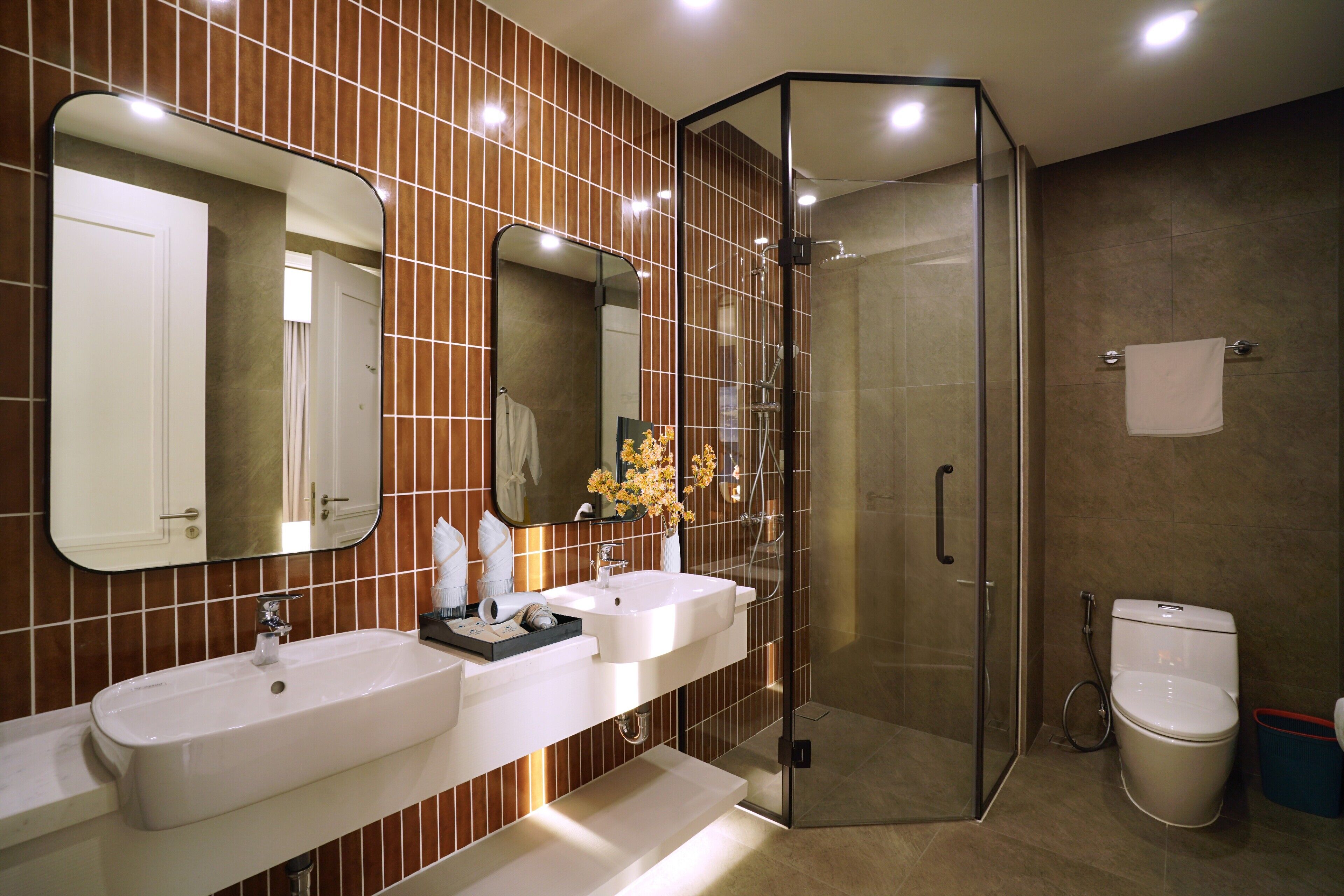 Un baño moderno con dos lavamanos, una ducha con cerramiento de vidrio y un inodoro.
