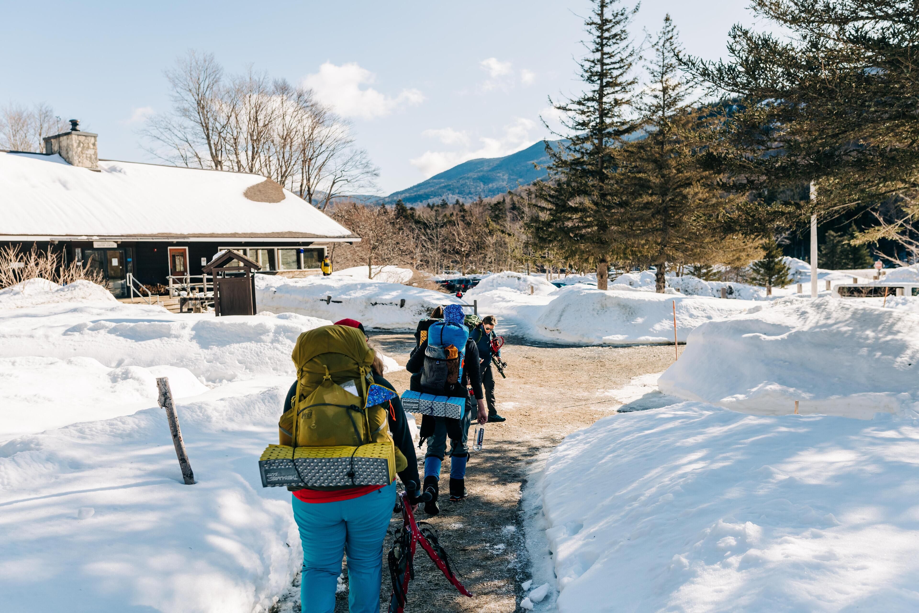 A snow-covered path leading to a building with a metal roof, surrounded by snowbanks and trees.