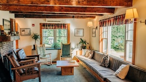 Un salon chaleureux avec une cheminée, des meubles en bois et de grandes fenêtres donnant sur l’extérieur.