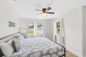 A bedroom with a bed, a ceiling fan, and large windows with curtains.