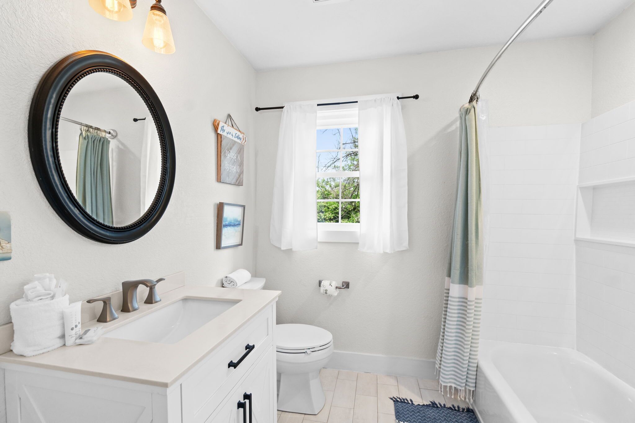 A modern bathroom with a large mirror, a bathtub, a toilet, and a window with curtains.