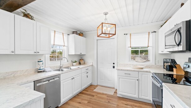 A modern kitchen with white cabinetry, a wooden floor, and a unique geometric pendant light. - Chasing Sunsets- Close to downtown, fenced yard, pet friendly, family friendly,Sleeps 9 (Port St. Joe)