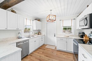 A modern kitchen with white cabinetry, a wooden floor, and a unique geometric pendant light. - Chasing Sunsets- Close to downtown, fenced yard, pet friendly, family friendly,Sleeps 9 (Port St. Joe)