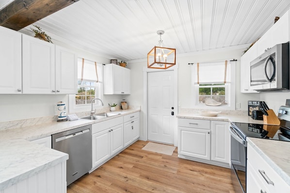 A modern kitchen with white cabinetry, a wooden floor, and a unique geometric pendant light.