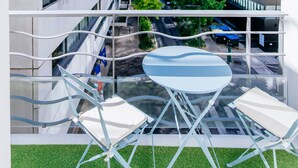 A modern building with a glass facade, a balcony with a table and chairs, and a view of the street below. - Paris Porte de Versailles -Metro (Issy-les-Moulineaux)