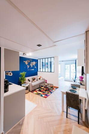Una sala de estar moderna con una pared azul de acento, un mapa mundial, un sofá, una mesa de centro y un comedor con una mesa y sillas blancas.