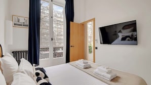 A hotel room with a bed, a TV, a window with curtains, a radiator, and a door leading to a balcony.