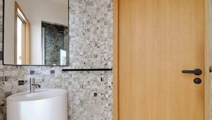 A bathroom with a marble mosaic wall, a white sink, and a wooden door.