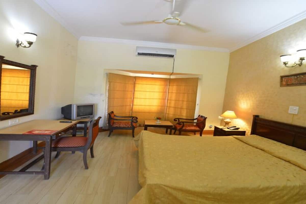 A hotel room with a bed, desk, chairs, and a television.