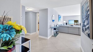 Ein modernes Wohnzimmer mit grauem Sofa, einem Glastisch und einem Flachbildfernseher, der eine Strandansicht zeigt.