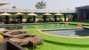 Piscina con sillas de descanso y sombrillas, rodeada de vegetación y un área de estar cubierta.