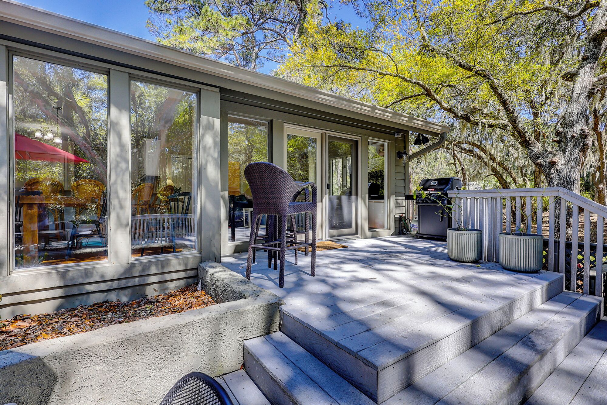 A covered outdoor area with a grill, chairs, and a view of the surrounding trees.