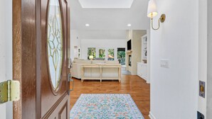 A spacious hallway with a wooden door, a floral rug, a sofa, and a television mounted on the wall.