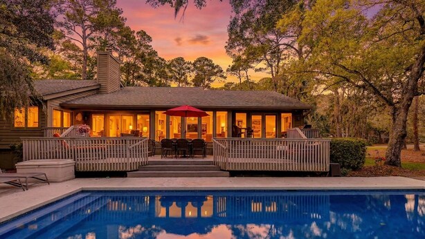 A house with a swimming pool, a covered patio, and a view of trees.