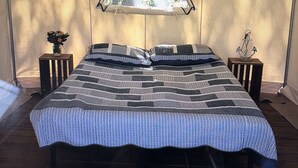 Een tent met een bed, twee nachtkastjes en een raam met uitzicht op bomen.