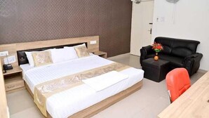 A hotel room with a large bed, a black leather sofa, a small table with a vase, and a wall-mounted fan. - Saalt Patliputra Hotel (Patna)