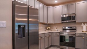 A modern kitchen with stainless steel appliances, grey cabinets, and a tiled floor. - Magical Moments Retreat: Your Family’s Gateway to Central Florida Fun (Kissimmee)
