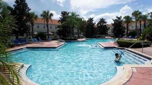 A swimming pool with a child swimming, surrounded by palm trees and lounge chairs. - Magical Moments Retreat: Your Family’s Gateway to Central Florida Fun (Kissimmee)