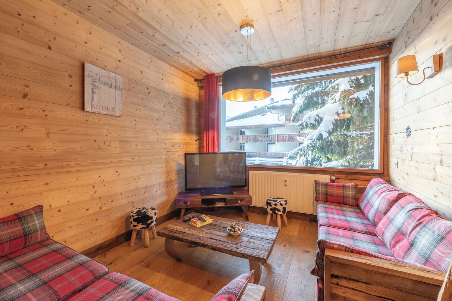A cozy wooden cabin interior with a sofa, a coffee table, a TV, and a window with a snowy view.